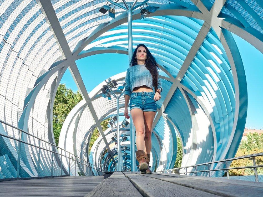 A young girl with dark hair knows what to wear to San Antonio Texas: she walks down a bridge as if it is a runway in her long sleeve grey top, denim shorts and cowboy boots.