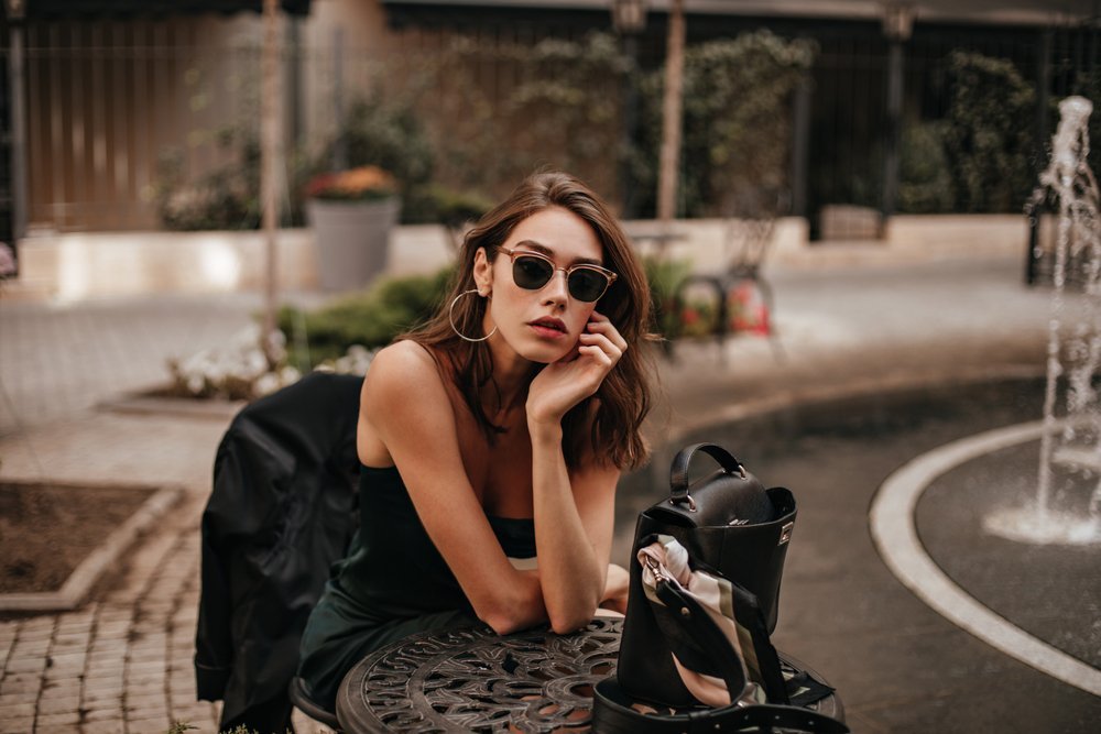 This model knows what to wear to San Antonio Texas for a night out: in a black, sleek, slip dress, she leans on a table and looks at the camera through her sunglasses, her black crossbody and silver hoops on full display.