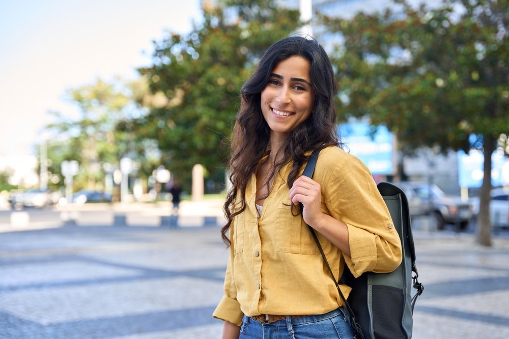 A woman knows what to wear to San Antonio Texas in her button down linen yellow shirt, jeans, brown belt, and backpack that keeps her hands free.