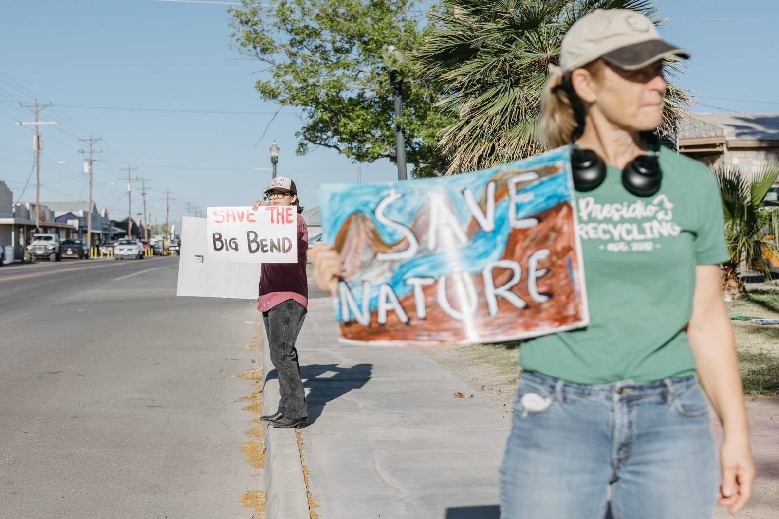 Protesters stand on a sidewalk alongside a road, holding signs that read “Save the Big Bend” and “Save Nature.”