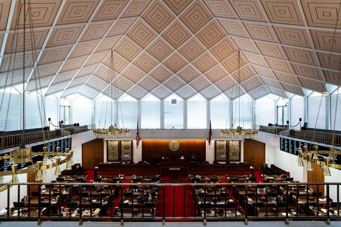 The interior of a spacious room with high ceilings, burgundy carpeting and rows of tables.