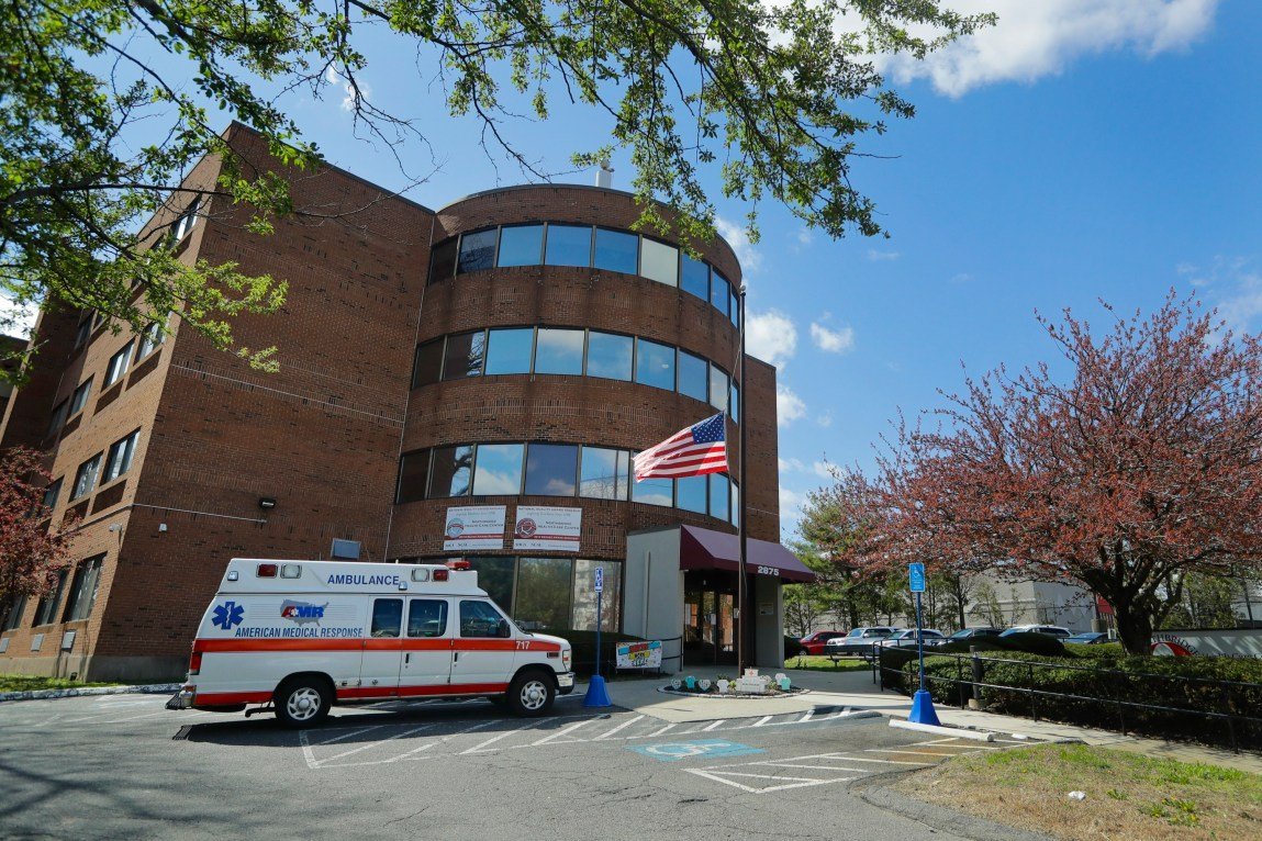 An ambulance parked outside a brick hospital building. An American flag flies at half staff outside the building.