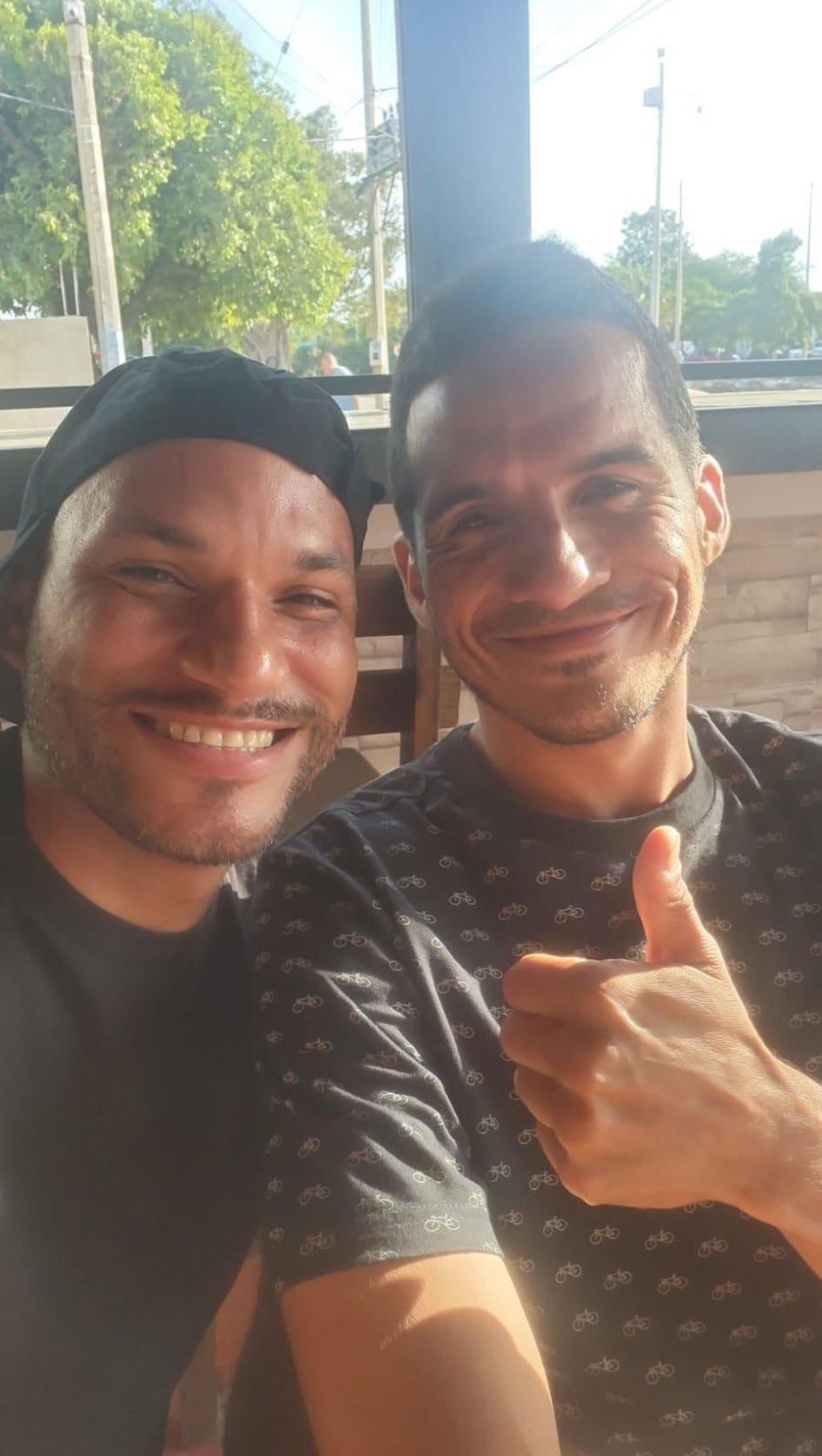 A selfie in which two men smile at the camera, one of them giving a thumbs-up.
