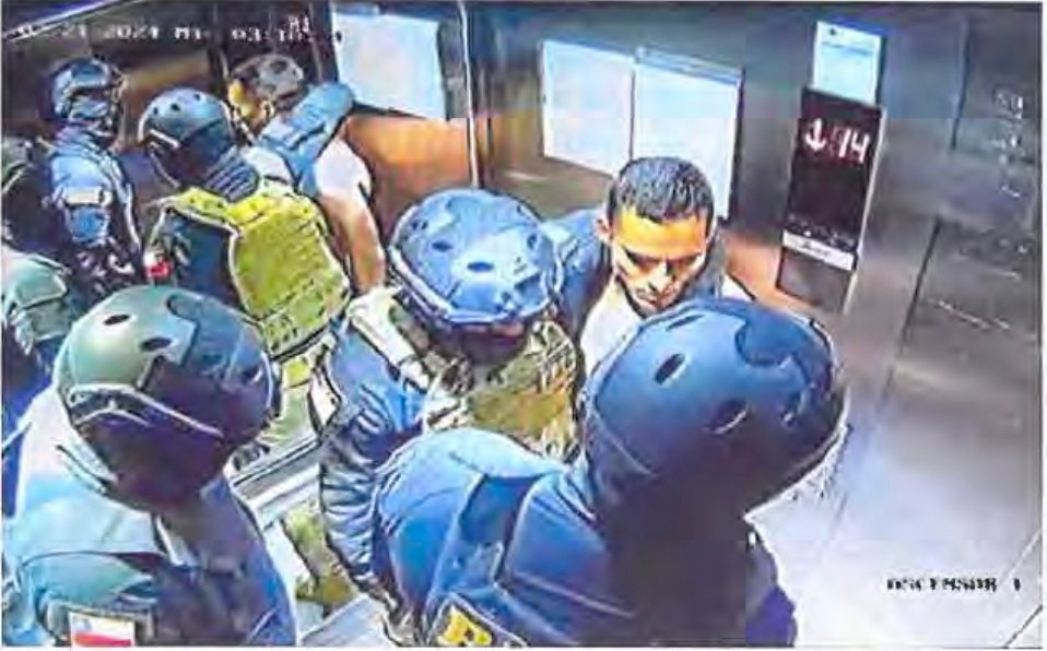 A group of men in tactical gear surround a shirtless man in an elevator.