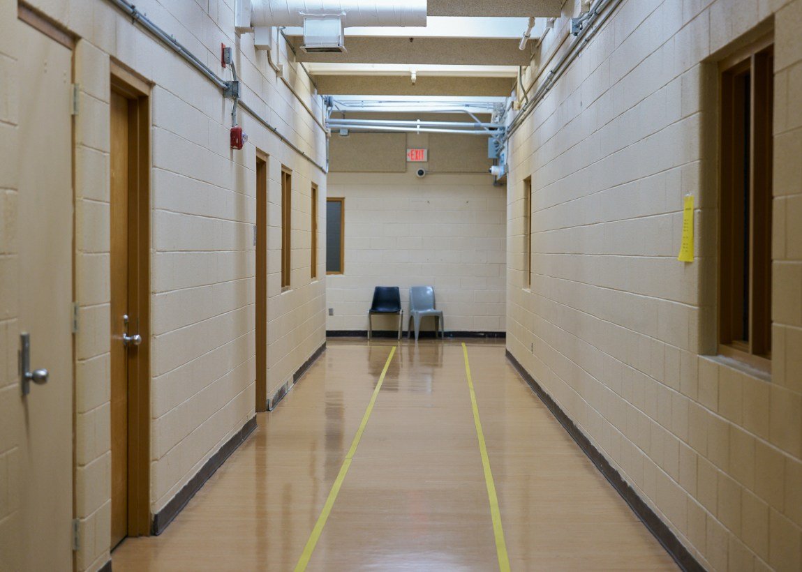 Two chairs sit empty at the end of a long hallway in an industrial-looking building.